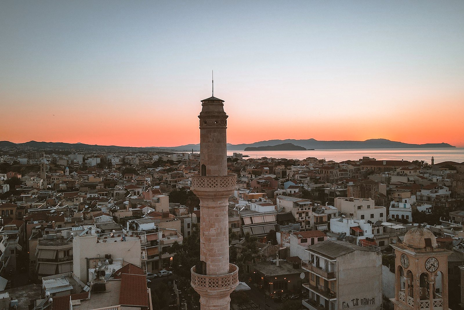 Sunset over the rooftops of Chania Old Town, with the stone minaret of Splantzia rising above the terraces and the sea beyond