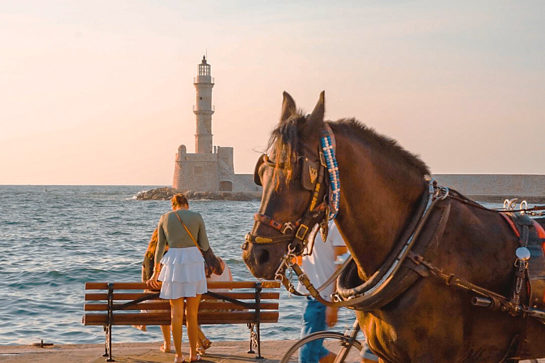 A horse-drawn carriage waiting on the Chania harbour front, the lighthouse across the water