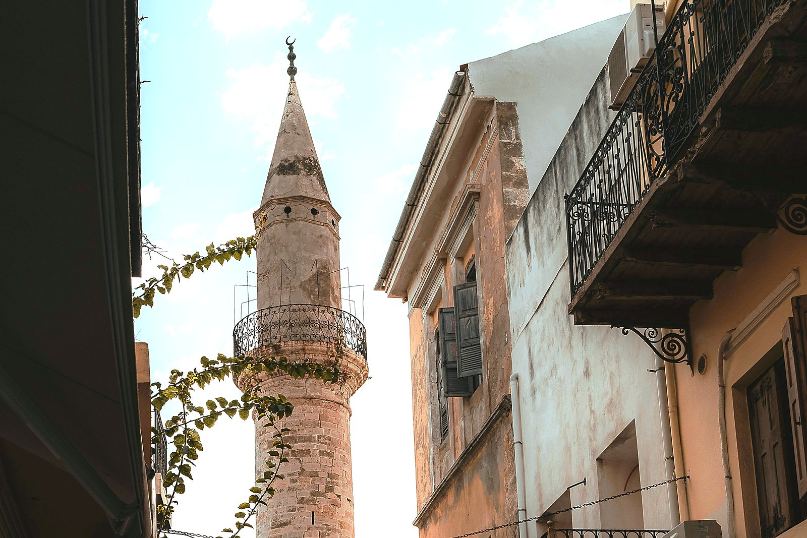 The Splantzia minaret seen from a narrow Old Town lane, between balconies and a climbing vine