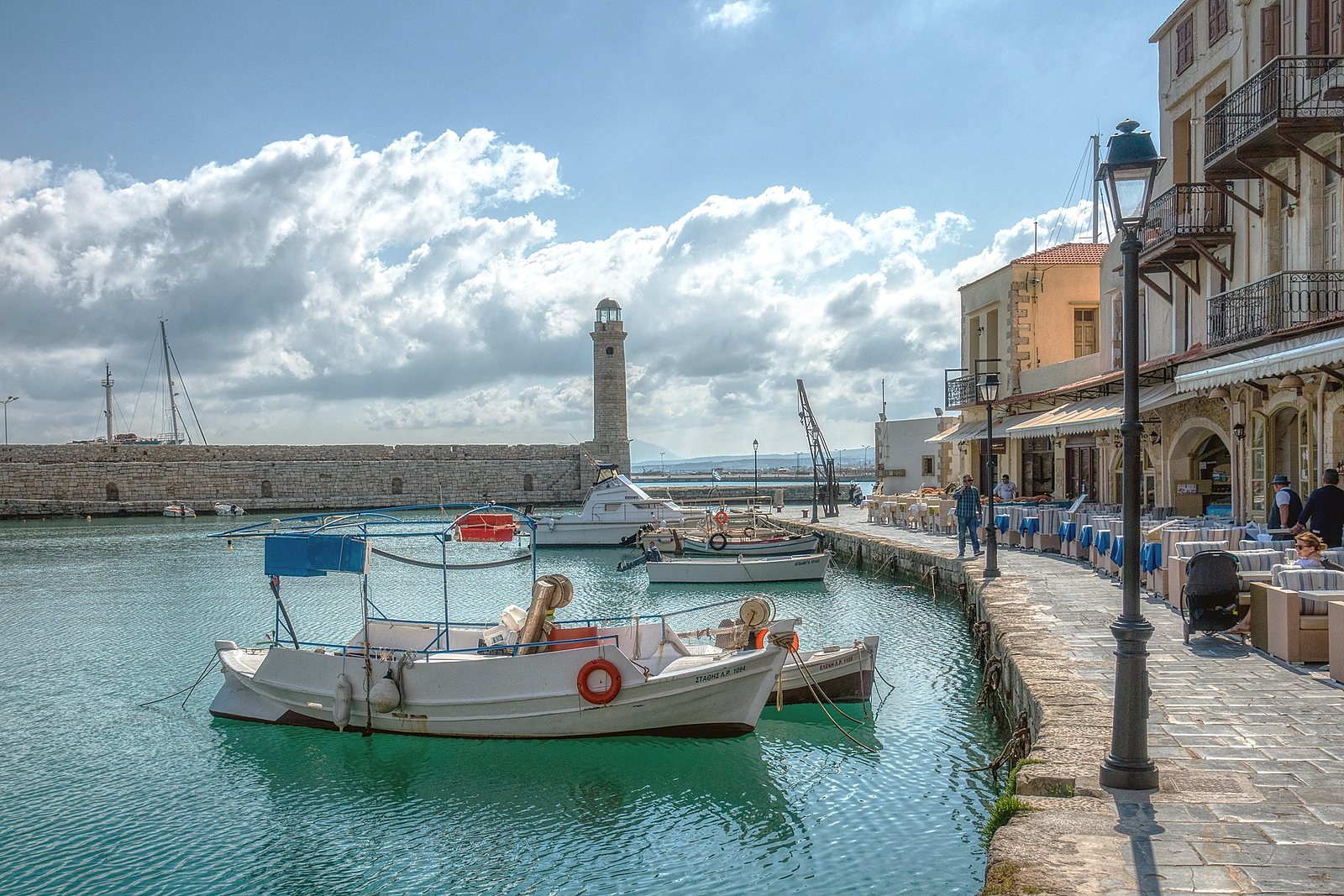 Fishing boats moored in the Venetian harbour at Rethymno, with the stone lighthouse and waterfront tavernas behind