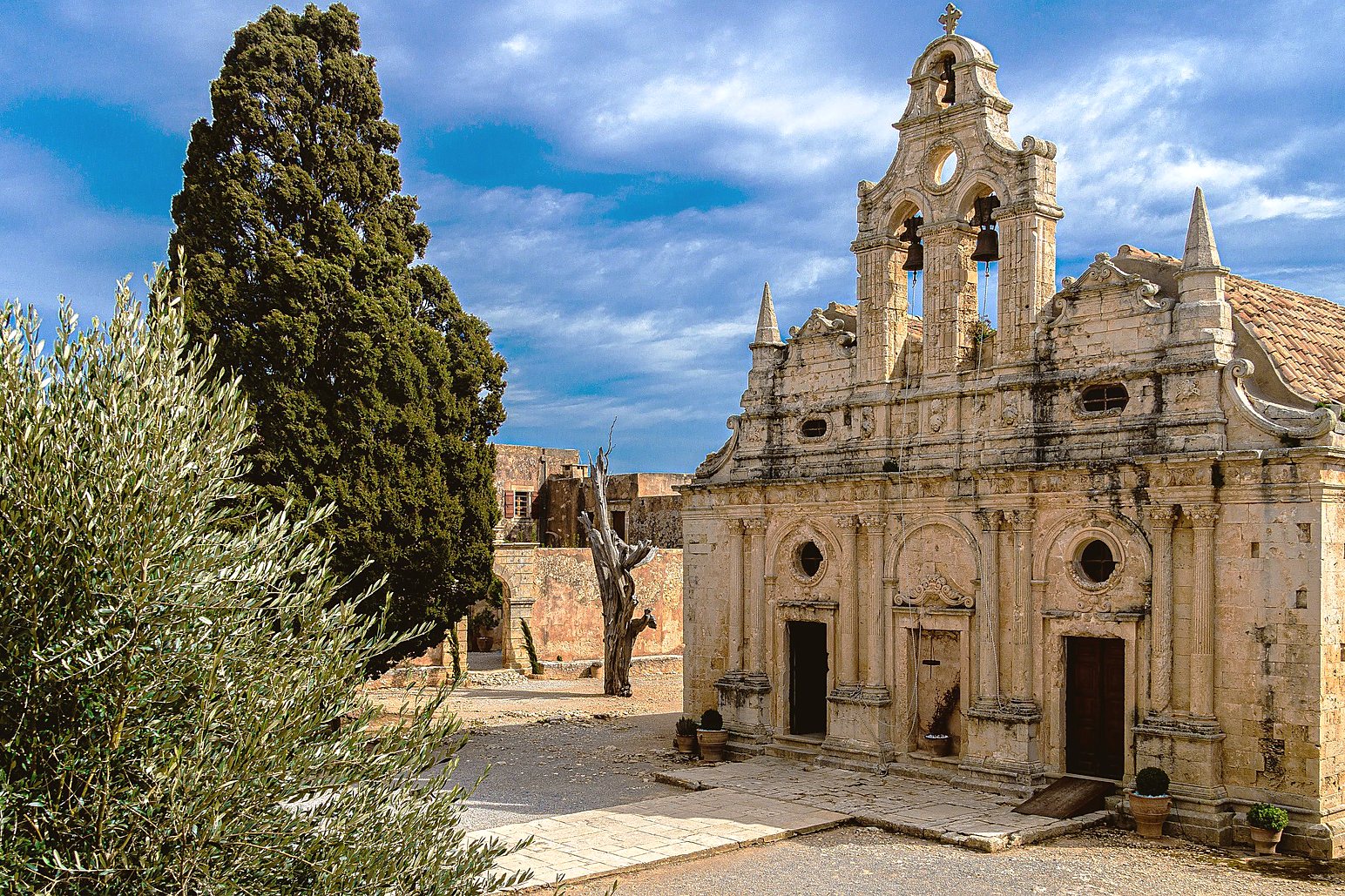 The carved Venetian facade and bell tower of Arkadi Monastery, framed by a cypress and an olive branch
