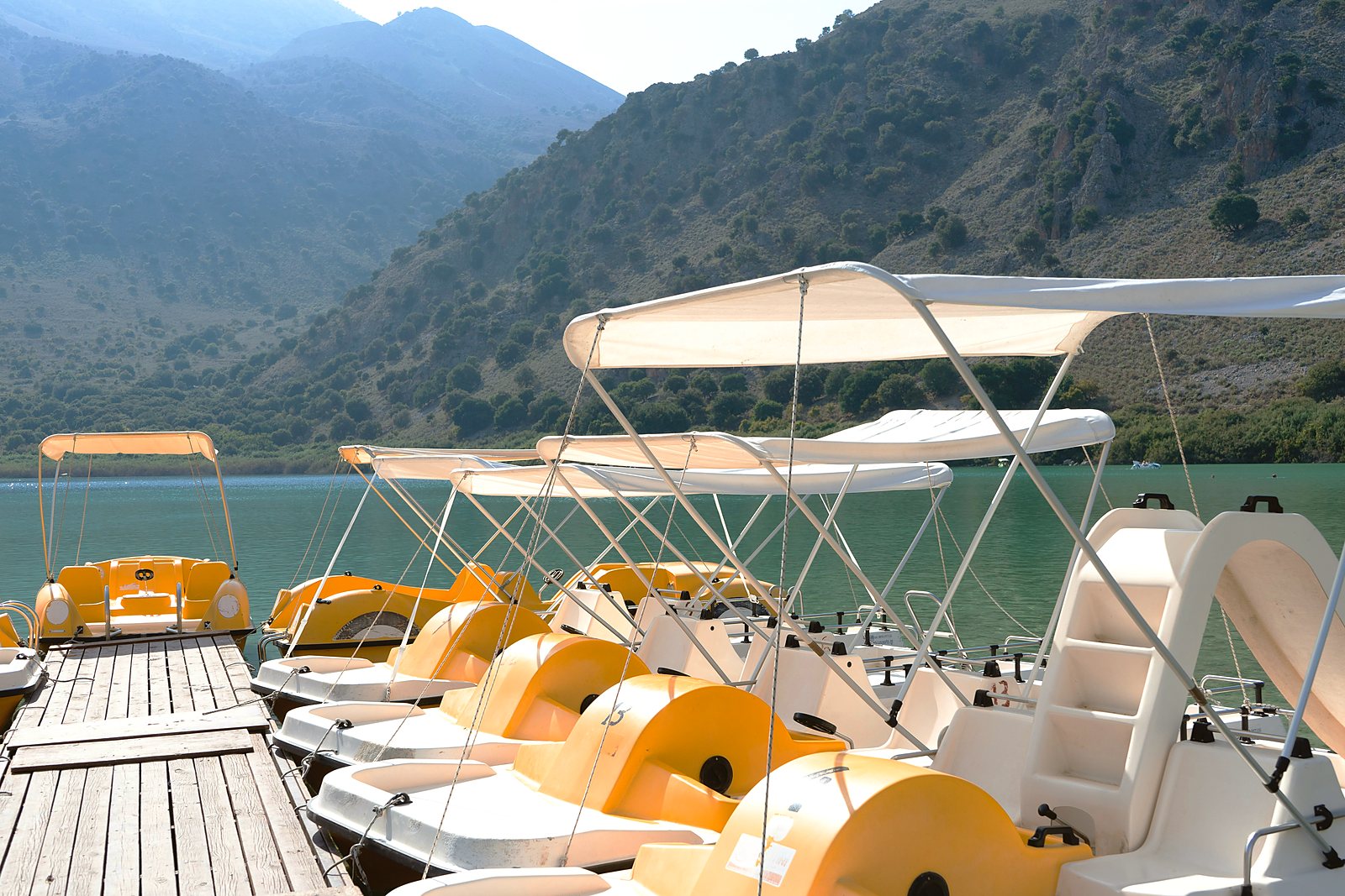 Pedal boats moored at the edge of Lake Kournas, with the wooded mountainside rising behind the water