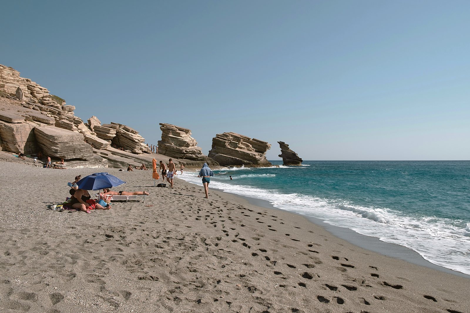 Swimmers on the sand at Triopetra, with the rock stacks that give the beach its name standing in clear water