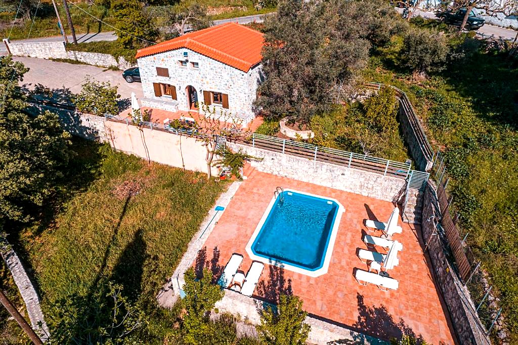 Aerial view of Horizon Villa Kastellos, a stone house with a terracotta roof beside its pool and terrace