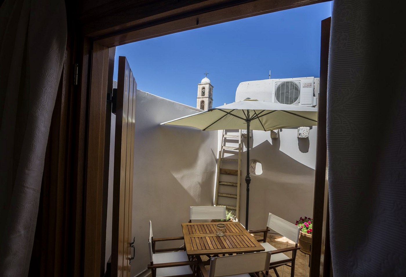 The private sun terrace at Horizon Sky House with a parasol, a church bell tower rising beyond